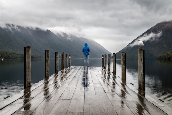 Man standing at end of pier looking out at misty lake